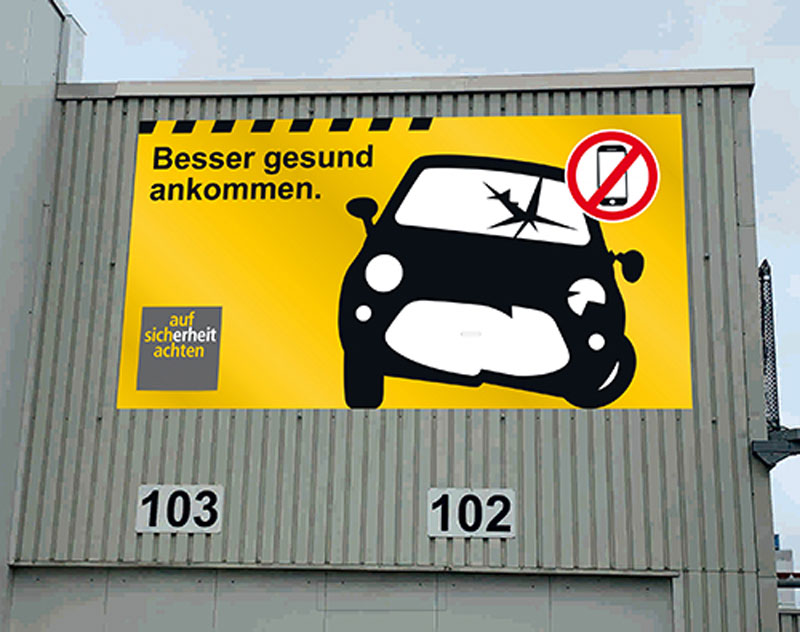 großes gelbes werbebanner an einer fabrikwand mit grafik eines unfallautos, jens sandrock, werbetechnik und netzwerkpartner 